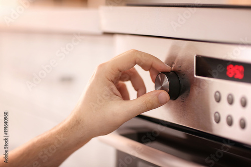 Man adjusting electric oven in kitchen, closeup