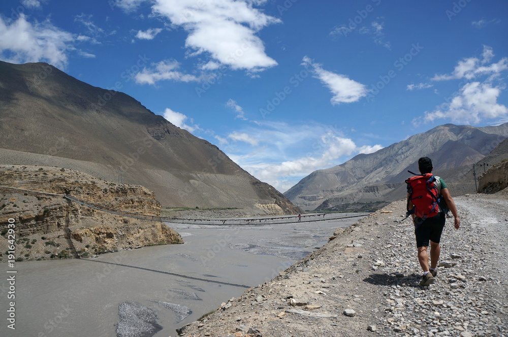 Tourist goes along the banks of the Kali Gandaki River, against the backdrop of the Himalayan mountains. Trekking to the closed zone of Upper Mustang. Nepal.
