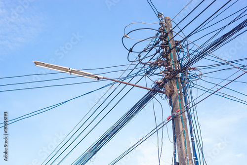 High voltage electricity pole and many wire of the cable line with blue sky and lamp on the pole.