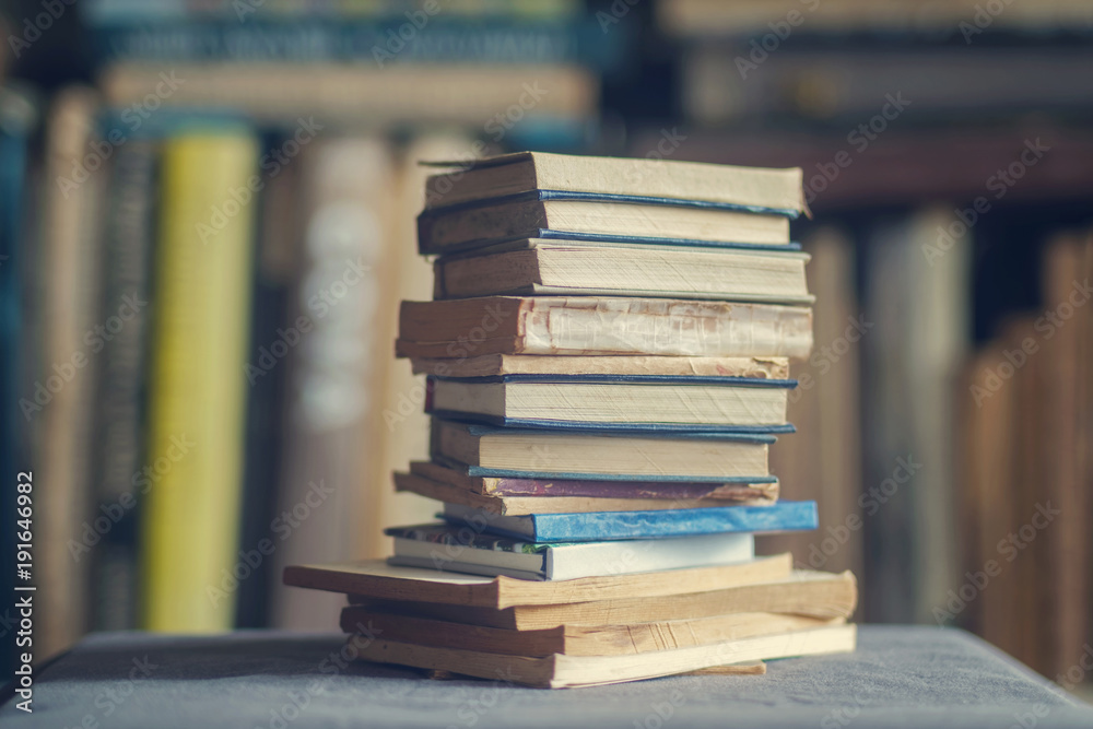 A stack of dusty shabby books in front of blurry shelves
