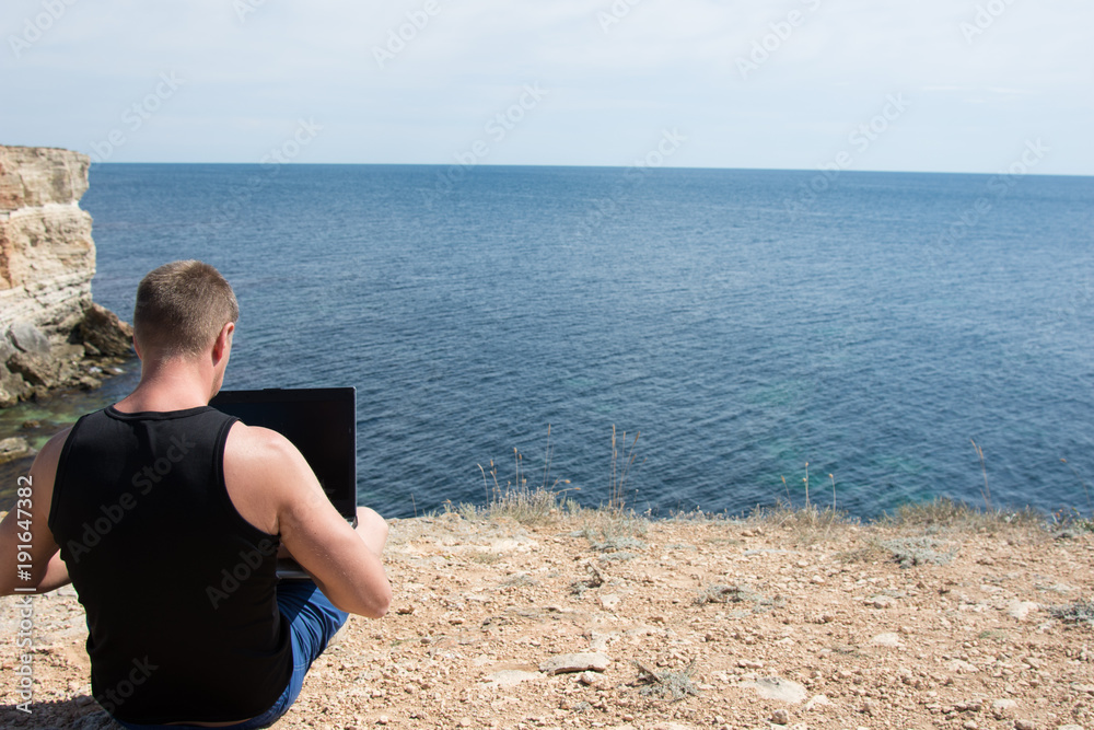 Summer, vacation. A man works for a laptop on the sea.