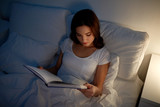 young woman reading book in bed at night home