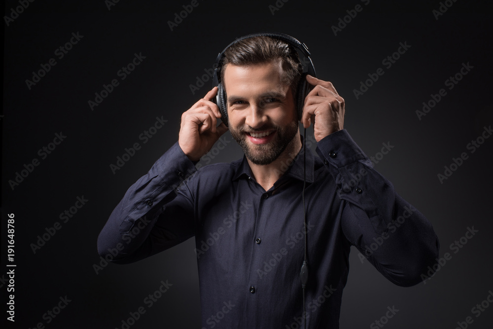 portrait of smiling man listening music in headphones isolated on black