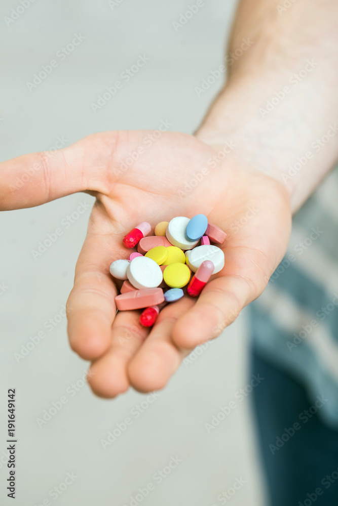 Closeup of a man holding colorful pills in his right hand