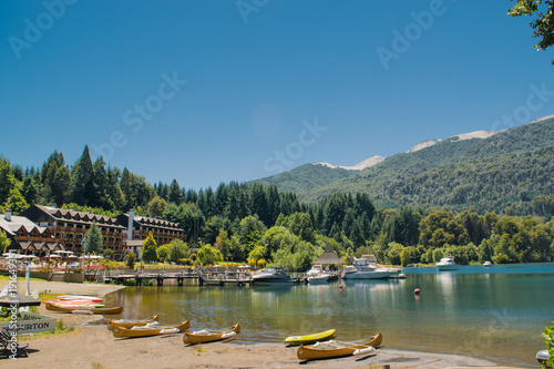Beach in front of turquoise lake with yellow canoes, boats and pine forest in the mountains