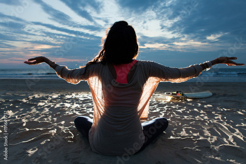 Fotografie Indian surfer girl with long hair sitting on the beach in lotus pose embracing l