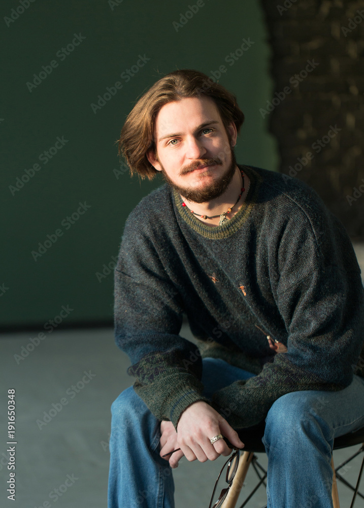 Fototapeta premium Portrait of hadsome young bearded stylish man sitting on the chair in studio