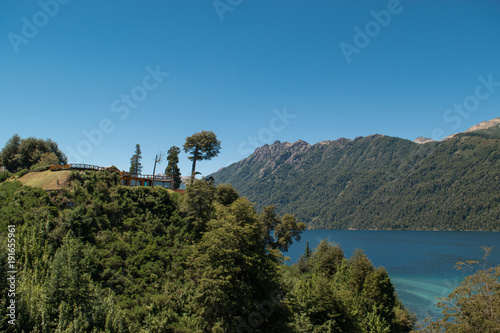 Landscape of a house on a hill facing a blue lake and mountains in the background