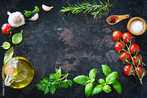 Olive oil, tomatoes, garlic, parsley, basil, spices on dark background