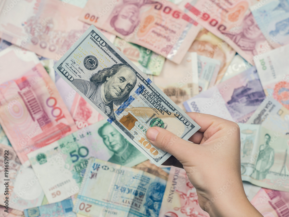 Obraz premium Female hand holding american hundred dollar bills over Asia money background. World Markets and Trade.