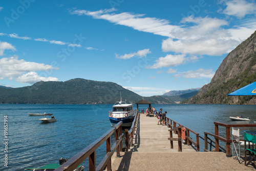 Blue lake with wooden pier, boats and mountains in background