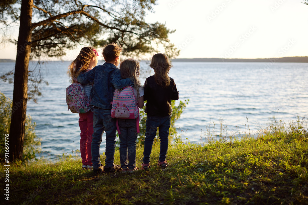 Four cute little sibling standing by the lake enjoying beautiful sunset view. Children exploring nature.