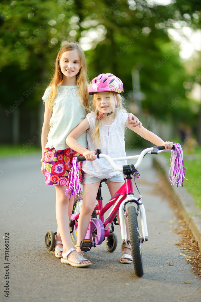 Small children learning to ride a bicycle in a city park on sunny summer evening. Cute little girls riding a bike.