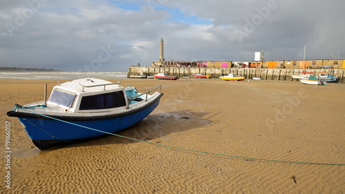 The beach at low tide with mooring boats and Margate Harbor Arm in the background, Margate, Kent, UK photo