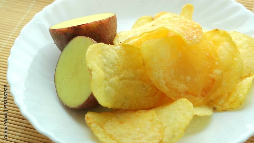 Homemade potato chips. Fast food. Popular junk food. Potato tubers and chips rotate smoothly on bamboo napkin. Diabetic diet. Homemade potato chips. Fast food. Popular junk food. Potato tubers and chips rotate smoothly on bamboo napkin. Diabetic diet.