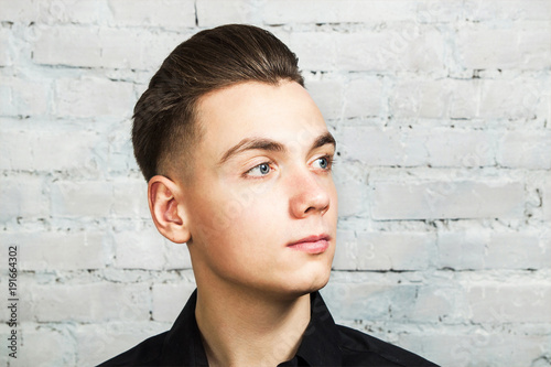 White young guy with pompadour hairstyle on a brick wall background.