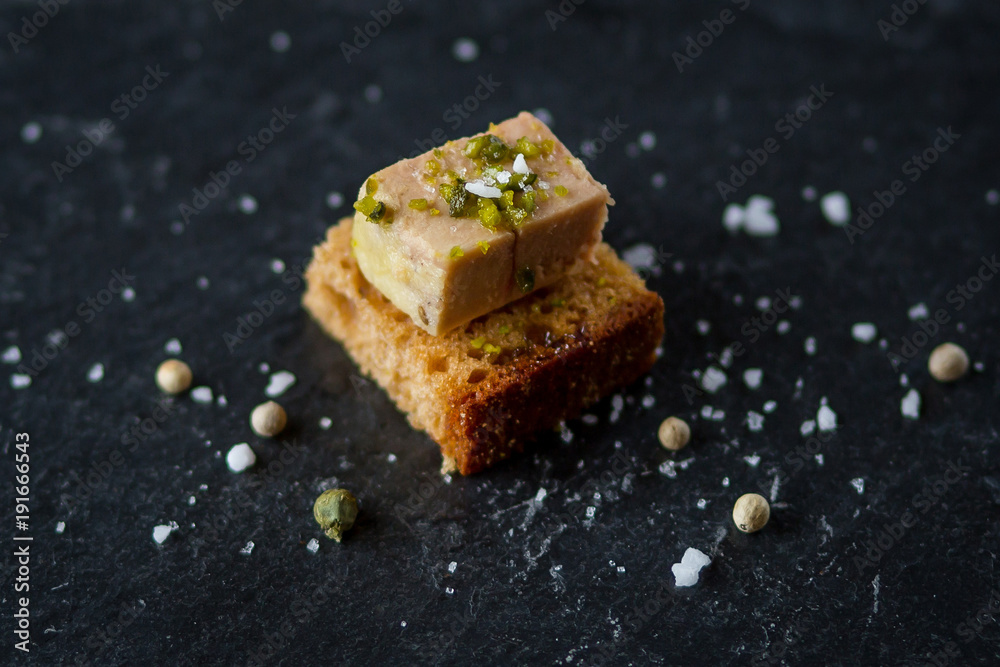 isolated foie gras toast on black plate with sea salt sprinkles