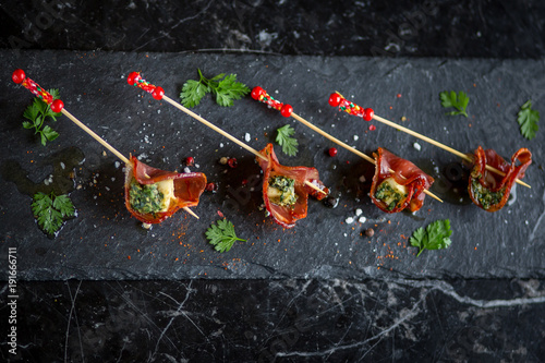parma ham and cheese skewers with olive oil on black plate with salt and peppercorns