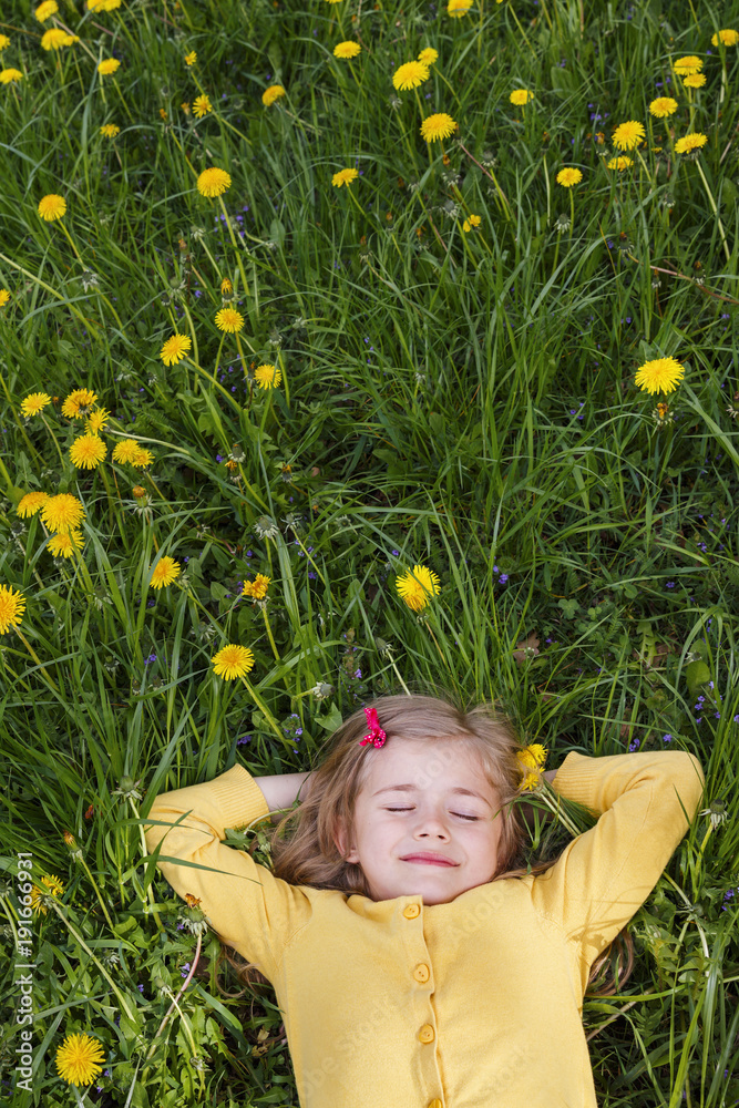 Happy little girl dreams on a green glade of dandelions Happy little girl dreams on a green glade of dandelions