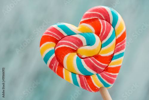 Sweet colored striped rainbow candy on a stick in the form of a heart. on a old vintage wooden background. The concept for Valentine's Day. Copy space. Place for your inscription photo