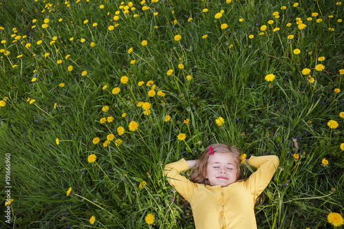 Happy little girl dreams on a green glade of dandelions