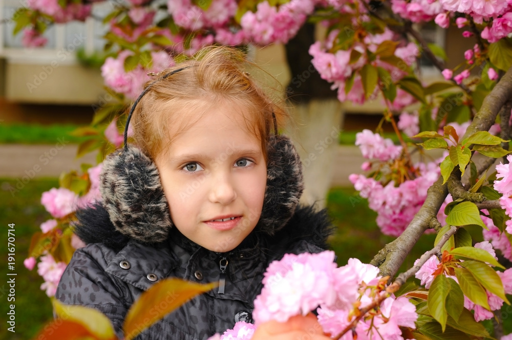 The young girl stands next to the blooming sakura in the spring The young girl stands next to the blooming sakura in the spring