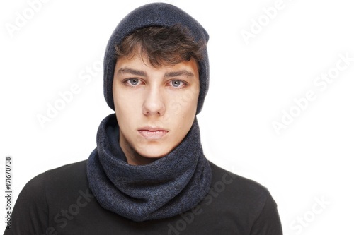 A handsome guy with a sad, angry face on a white background. He is wearing a warm cap and a scarf