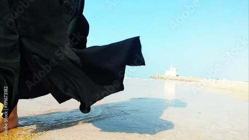 Woman wearing abaya walking on the beach on a sunny day photo