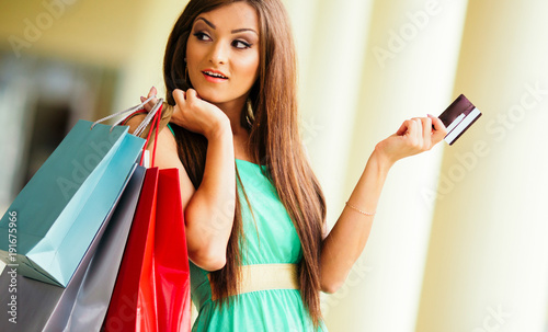 stunning and very beautiful woman in dress with long brown hair holding card and colored shopping bags