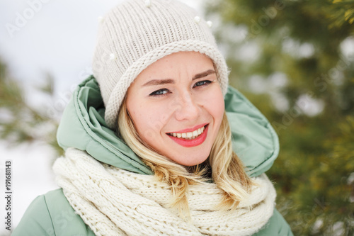 Portrait of a beautiful attractive girl outdoors in winter. The girl looks at the camera and smiles. Close-up.