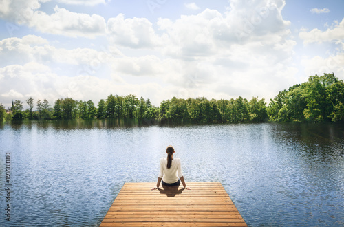 Woman relaxing on wooden dock by a beautiful lake. Peace and tranquility in nature. 