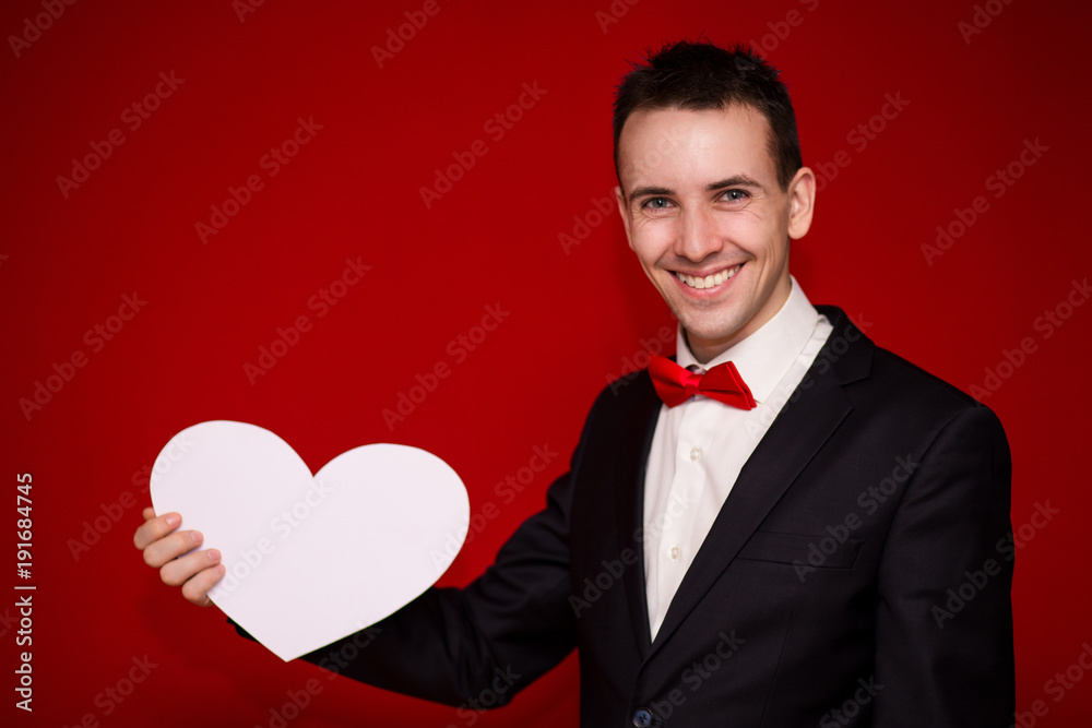 Stylish man in suit hold white paper heart on red backgroundt. Valentines day composition Stylish man in suit hold white paper heart on red backgroundt. Valentines day composition