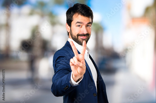 Handsome man making victory gesture on unfocused background