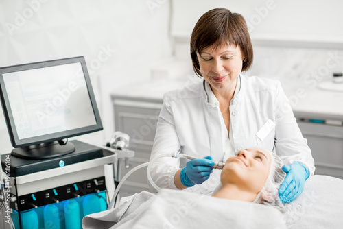 Senior woman cosmetologist making facial procedure to a young client in a luxury medical resort office