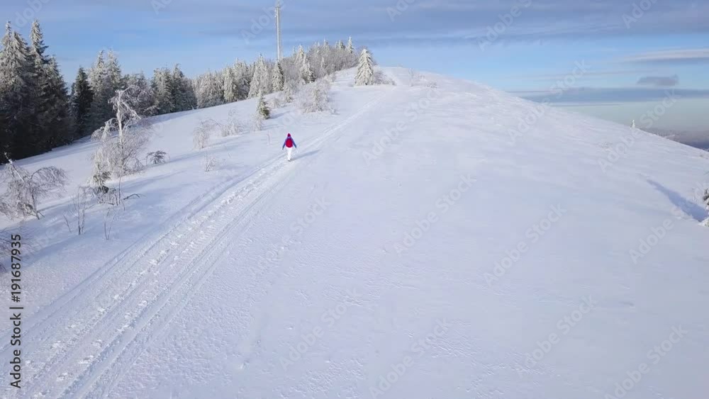Flight over the lonely tourist girl walking along the top of a mountain covered with snow. Clear frosty weather Flight over the lonely tourist girl walking along the top of a mountain covered with snow. Clear frosty weather
