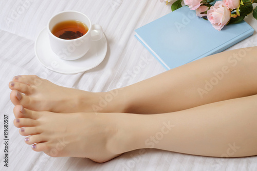 Female feet in bed book tea flowers