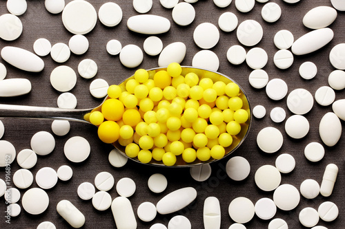 Yellow vitamins in spoon and white medicine pills