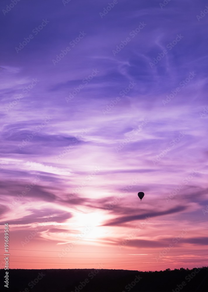 Hot air balloon flies in colorful evening sky
