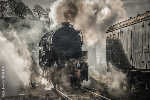 Φωτογραφία A early morning back lit photograph of a steam train smoking and letting off ste