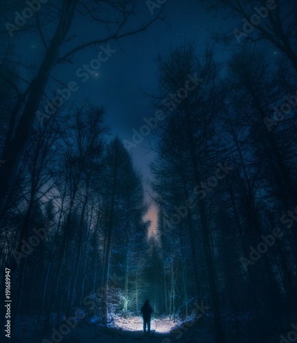 Surreal night forest landscape with alone strange man with flashlight.