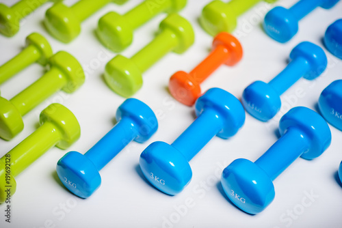 many blue green and one orange in the middle dumbbells on a white background ,concept preparing to fitness sports equipment top view mock up
