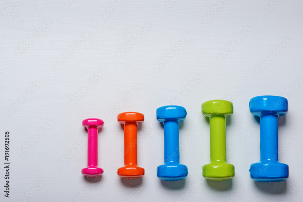 many blue green and one orange in the middle dumbbells on a white background ,concept preparing to fitness sports equipment top view mock up