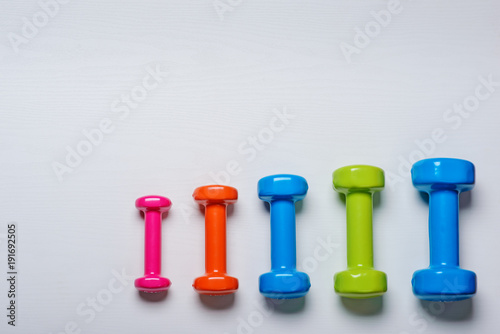 Obraz na płótnie many blue green and one orange in the middle dumbbells on a white background ,concept preparing to fitness sports equipment top view mock up w salonie