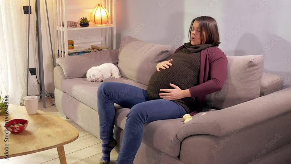 Pregnant woman having contractions on sofa at home wide shot Pregnant woman having contractions on sofa at home wide shot