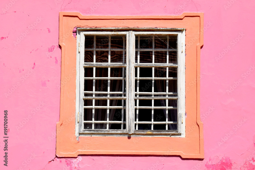 White window and pink wall. White wooden window in pink wall. Old building. Metal lattice.