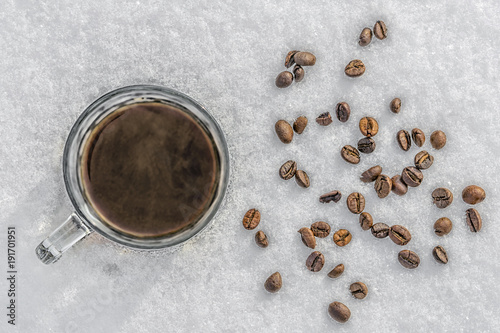 hot mug of black coffee in cold snow, coffee beans scattered