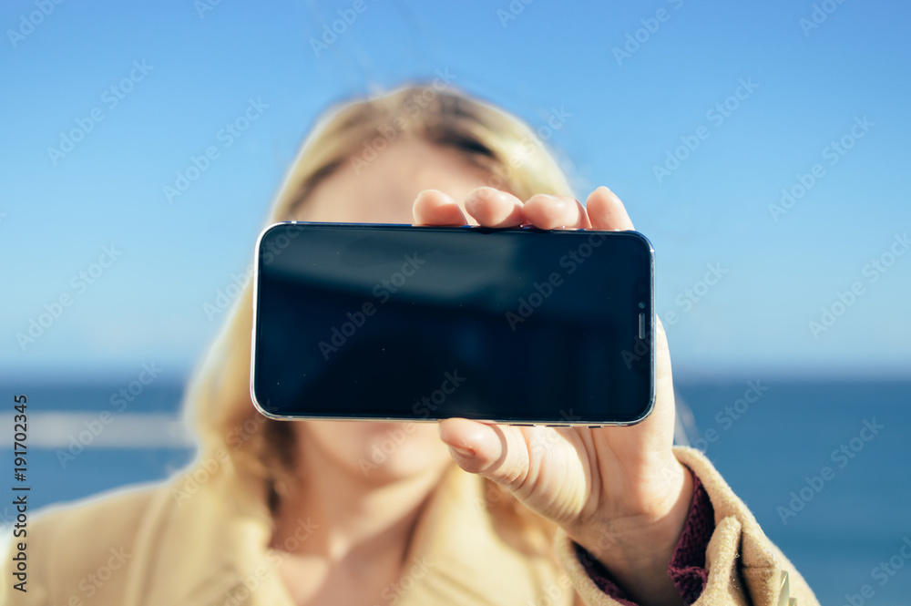 Closeup view of person holding using mobile smart phone. Sunny day outdoor. Back side top view display mock up design background of texting, talking, GPS navigation, modern communication technology