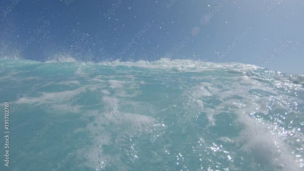 LOW ANGLE VIEW: Cool male surfer in black and blue wetsuit makes a sharp turn on his surfboard. Surfer carves awesome ocean wave and splashes clear water on camera. Young adult having fun surfing.