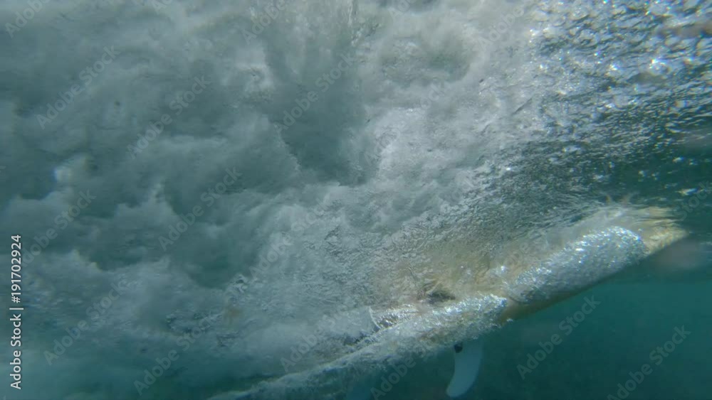 LOW ANGLE, UNDERWATER: Enthusiastic young surfer riding a fast barrel wave in sunny Lobos. Sportsman on surfboard in black wetsuit speeds past camera on awesome ocean wave. Man having fun surfing.