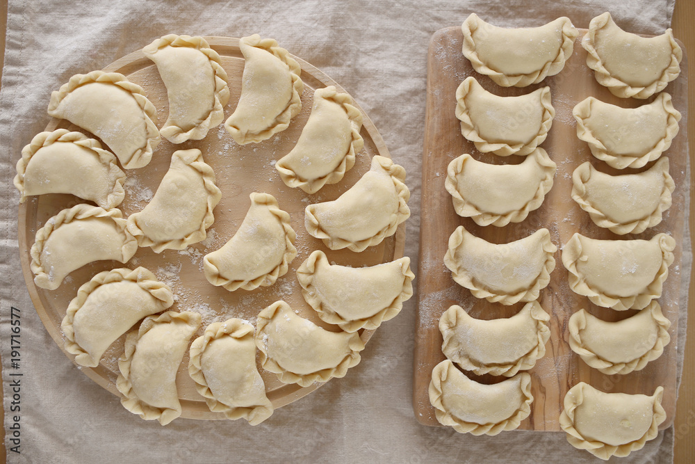 Dumplings raw on a wooden round board on a linen beige napkin. Traditional homemade food. traditional dish of Russian and Ukrainian cuisine